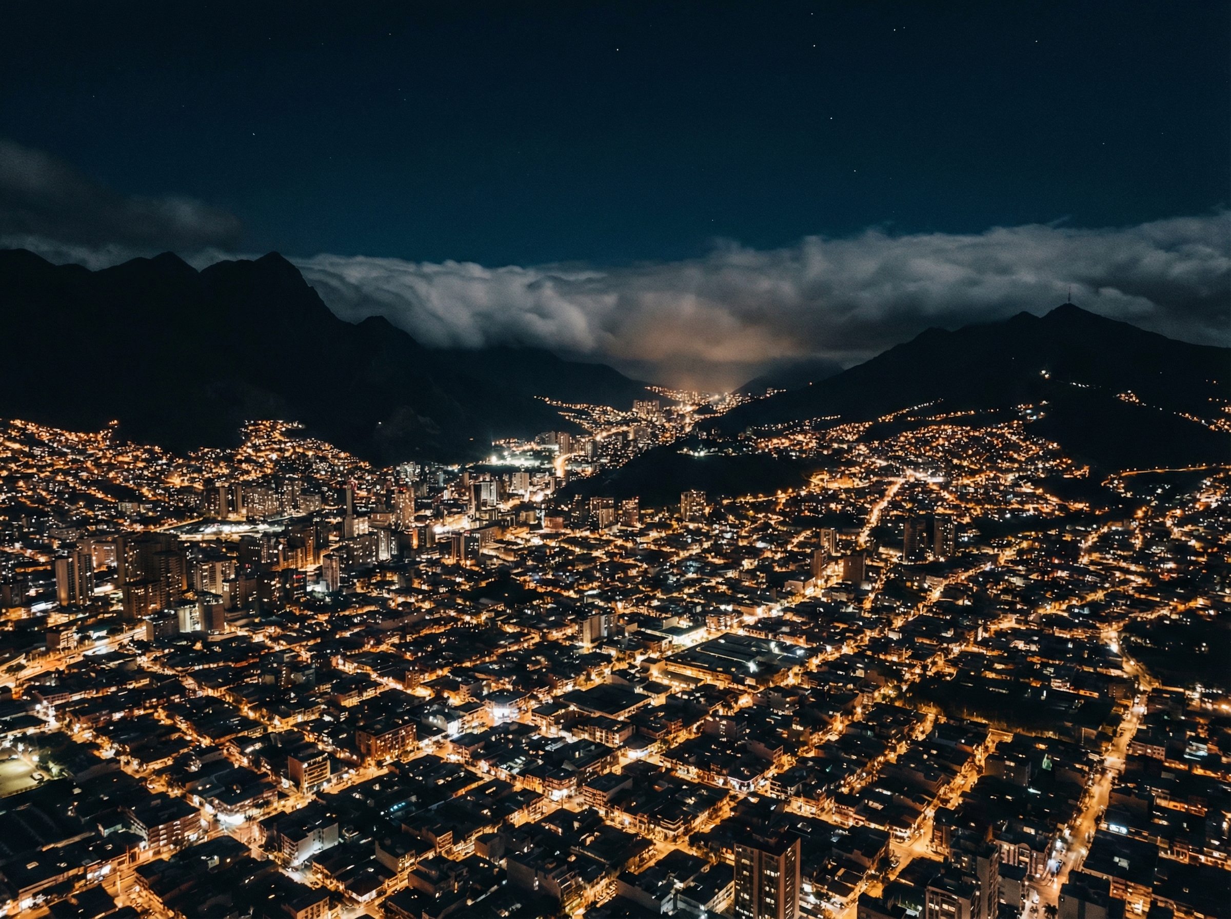 An aerial view of a dense South American city at night with warm city lights and dark mountain silhouettes in the background, a moody and atmospheric landscape, high contrast, 4:3 aspect ratio, no text